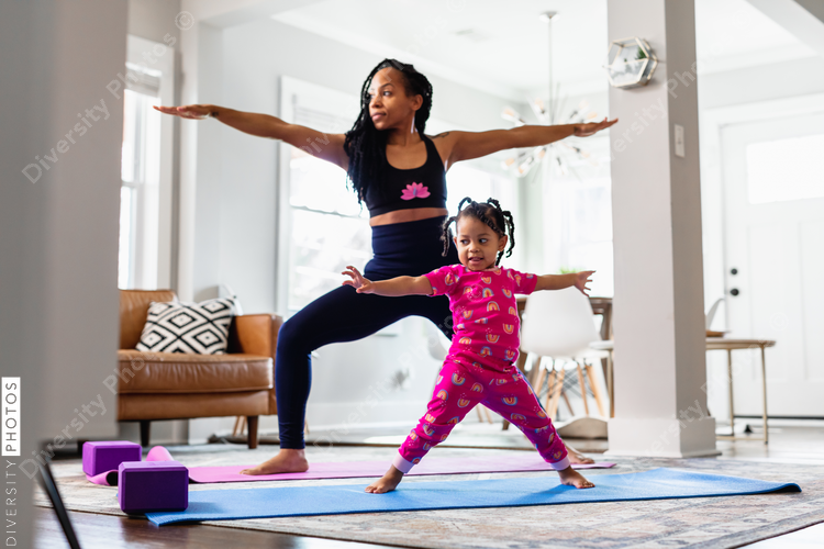 Black Mother and daughter doing yoga in family room, warrior pose