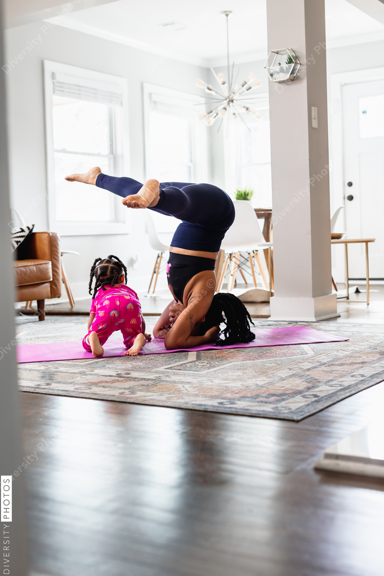 Woman does headstand with daughter playing in family room