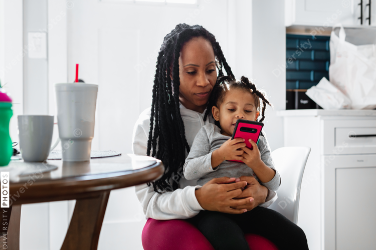Toddler watches television show on phone sitting in mother's lap