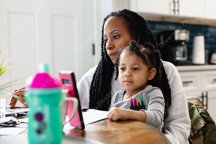 Black woman working from home with toddler child sitting on lap