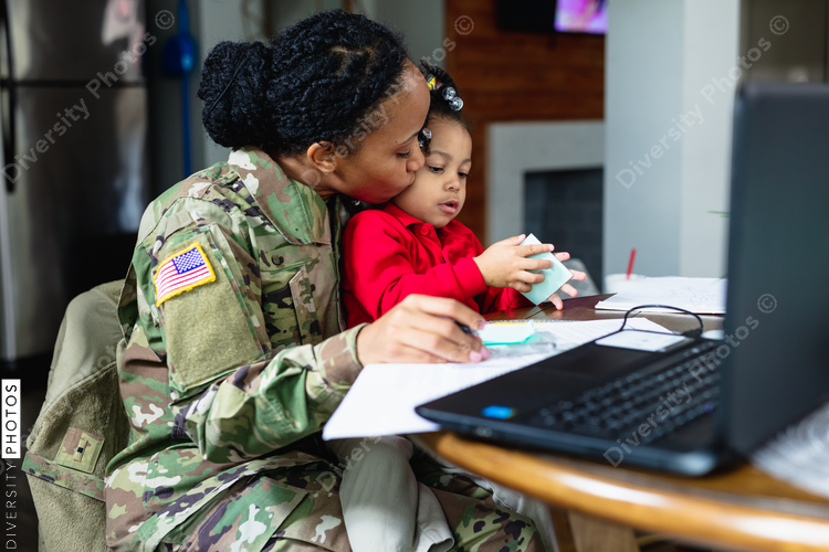 Black soldier mother kisses daughter while working from home