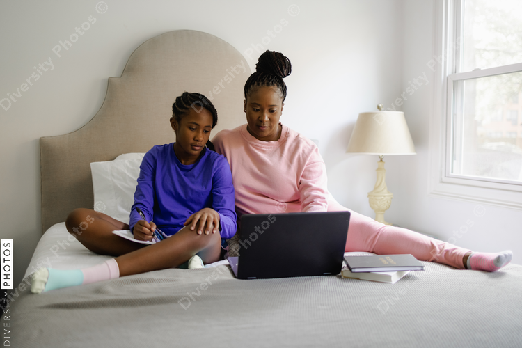 Black Mother and teenage daughter using laptop on bed