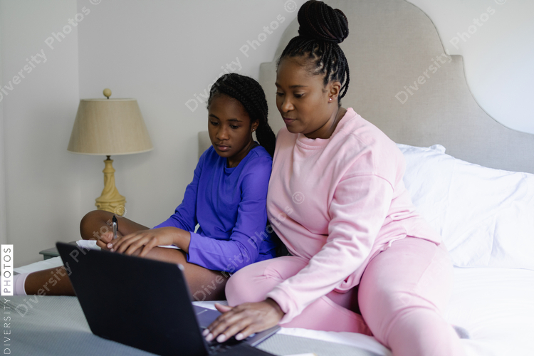African American Mother and teenage daughter using laptop on bed