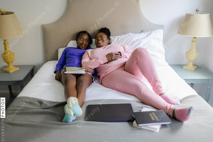 Smiling mother and teenage daughter lying on bed, African American