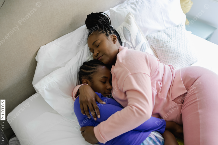 Overhead view of mother and teenage daughter embracing on bed