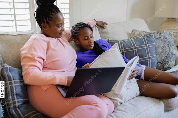 Woman using laptop and teenage daughter studying on sofa in living room