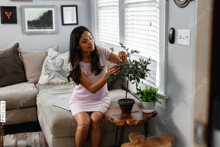 Indian woman inspecting house plant indoors, comfortable clothing