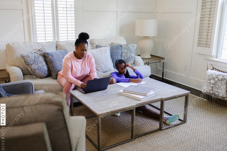 Teenage girl doing homework¬†and mother using laptop at table in living room