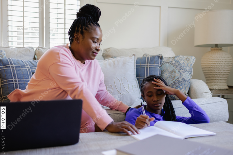 African American Mother assisting teenage daughter doing homework at table in living room