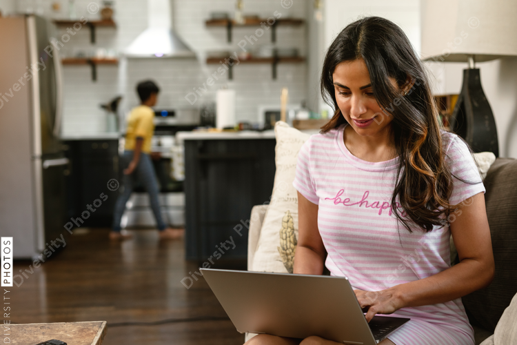 Indian mom working from home laptop while son in kitchen in the background