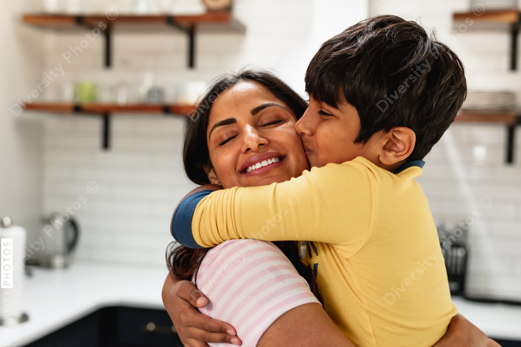 Smiling Indian mom embracing son at home in kitchen