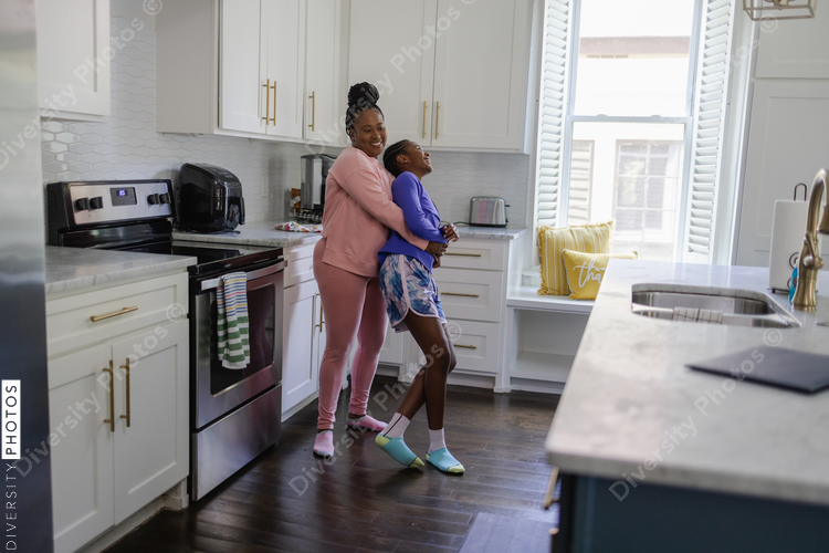 Happy mother and teenage daughter embracing and laughing in kitchen, African American