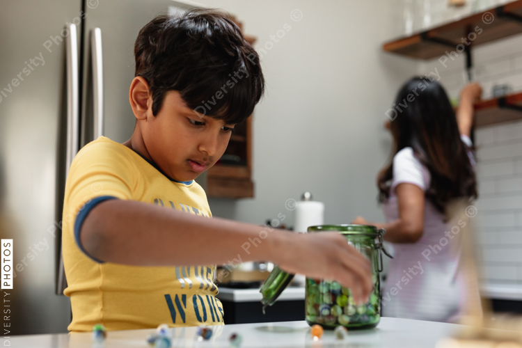 Indian boy playing with marble toys while mom is in the background in the kitchen