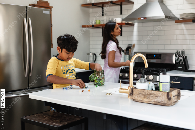 Indian boy playing with marble toys while mom is in the background in the kitchen
