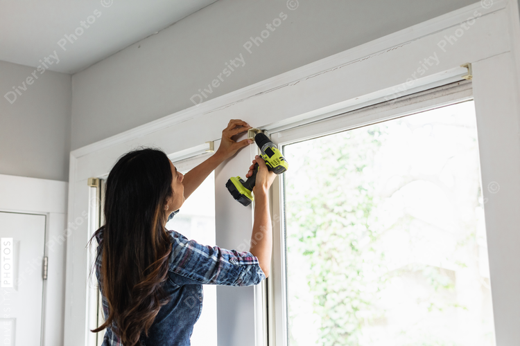 Indian woman using drill power tool to install blinds, DIY home improvement project