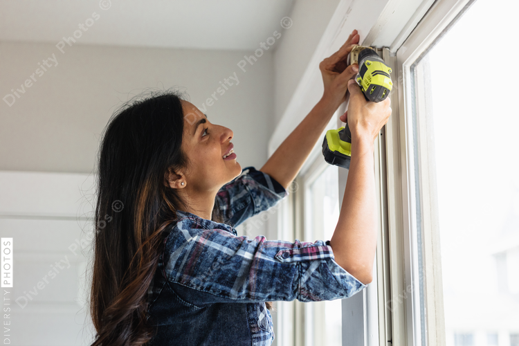 Indian woman using drill power tool to install blinds, DIY home improvement project