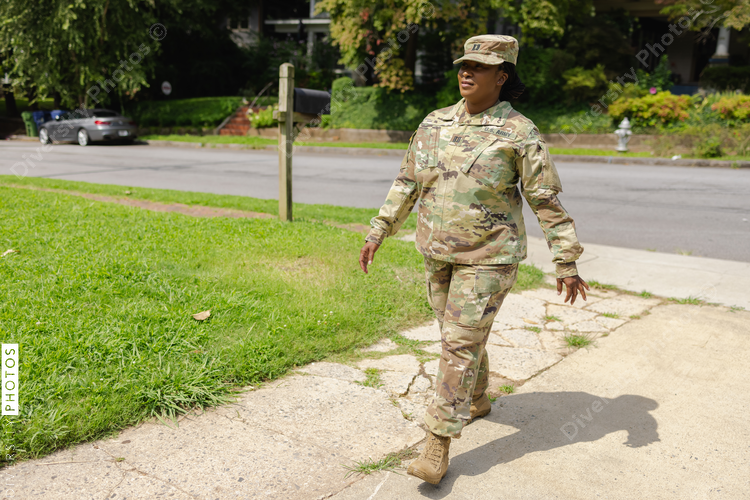 Military woman in camouflage uniform walking on front yard