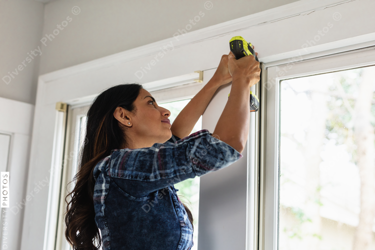 Indian woman using drill power tool to install blinds, DIY home improvement project