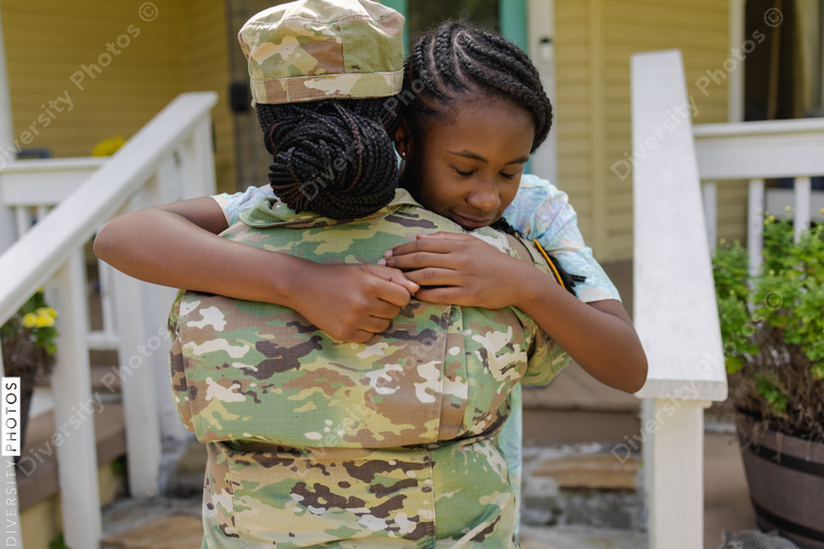 Black Military woman in camouflage uniform hugging daughter in front of house