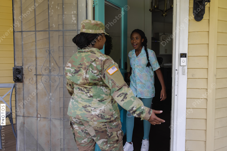 Happy teenage girl greeting military mother in camouflage uniform in doorway
