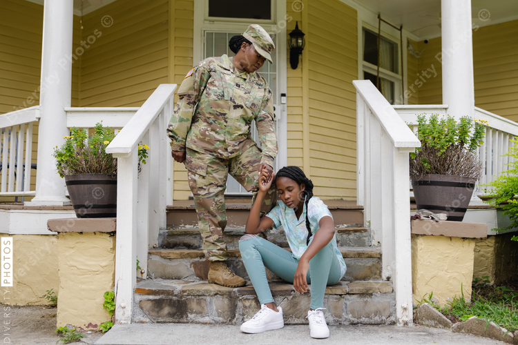 Military woman in camouflage uniform with teenage daughter on steps in front of house