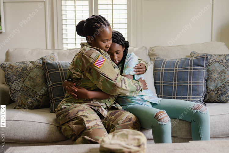 Military woman embracing sad daughter on sofa