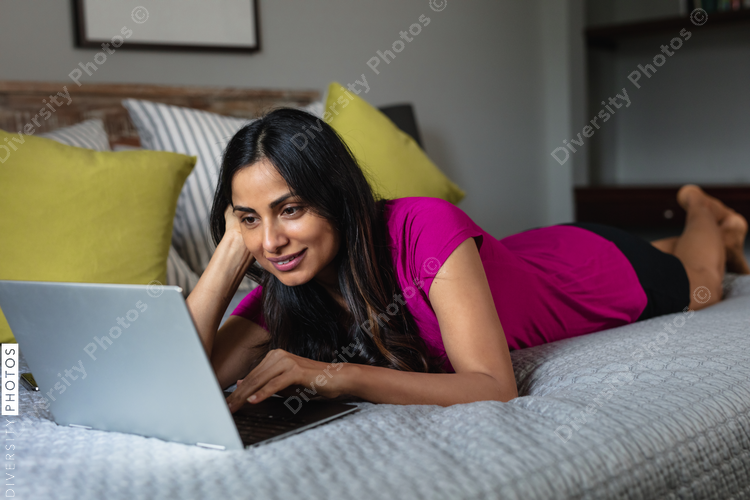 Indian woman comfortable at home in bed on laptop, remote working
