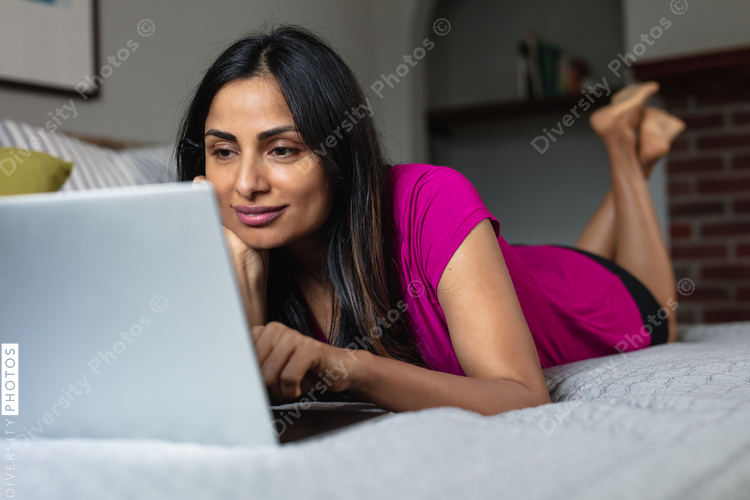 Indian woman comfortable at home in bed on laptop, remote working