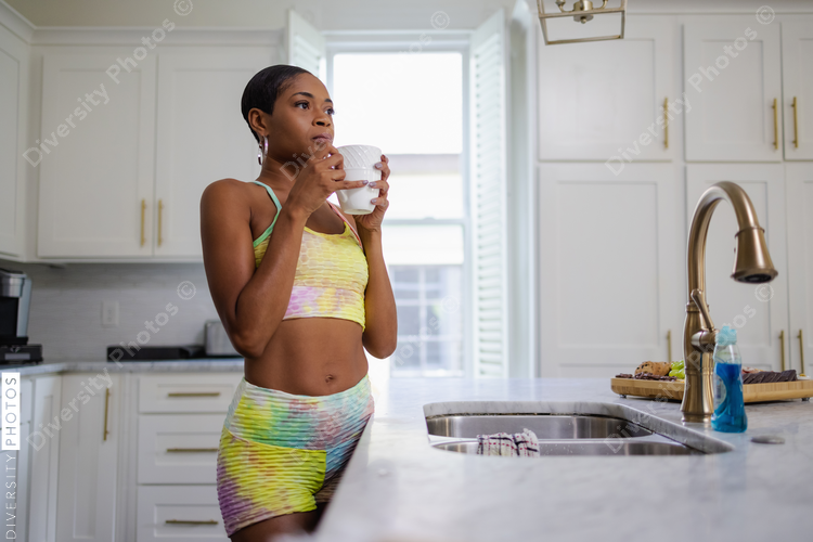 Woman in sports bra drinking coffee in kitchen