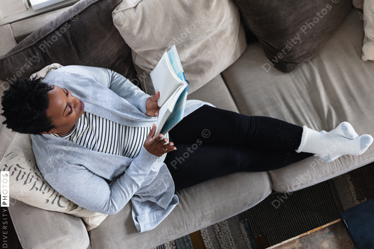 African American woman reading book at home on couch, cozy and comfortable