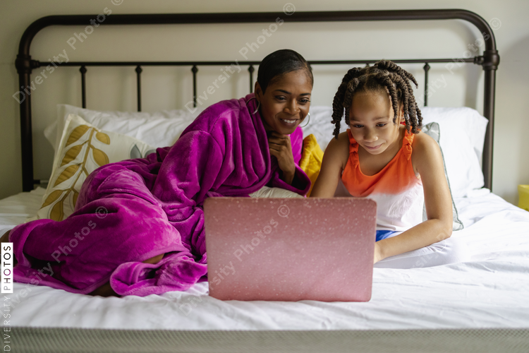 Mother and daughter sitting on bed looking at laptop