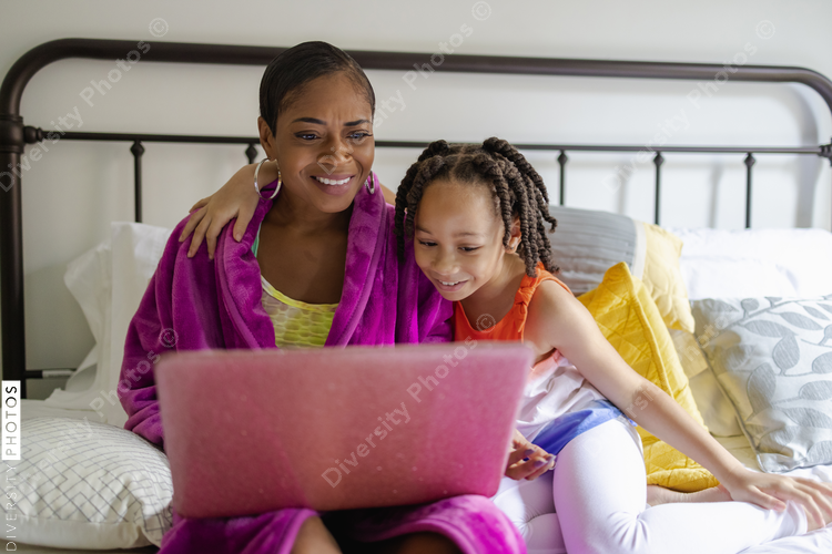 Mother and daughter sitting on bed looking at laptop