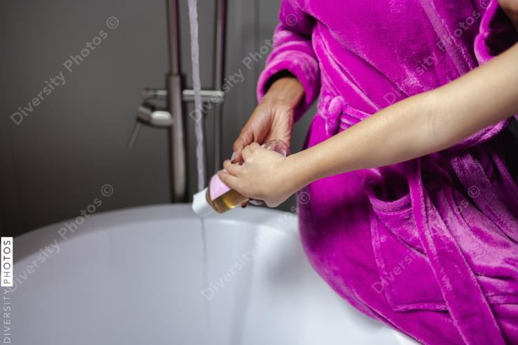 Mother and daughter pouring shower oil into bathtub