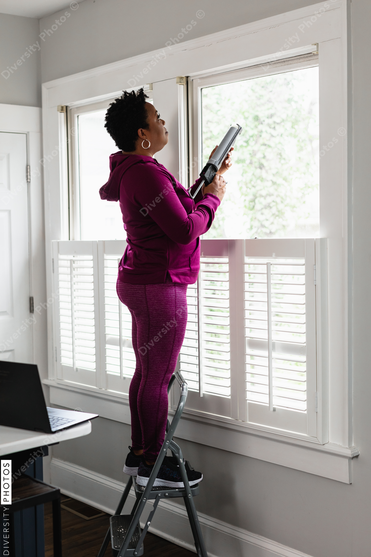 Black woman caulks window sill, energy efficiency, home improvement, DIY