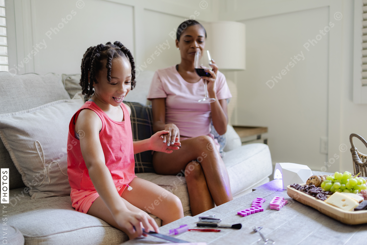 Mother and daughter sitting on sofa, looking at nail polish kit
