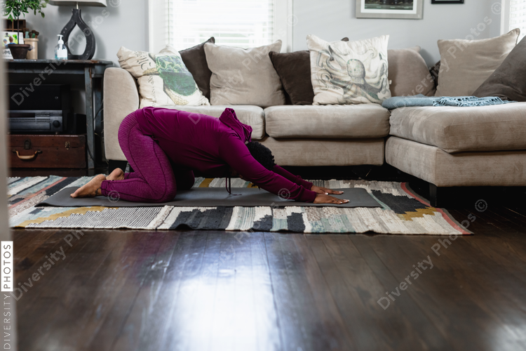 Black woman doing childs pose at home in living room, yoga flow