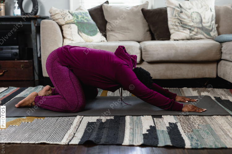 Black woman doing childs pose at home in living room, yoga flow