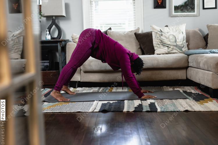 Black woman does downward dog yoga pose at home