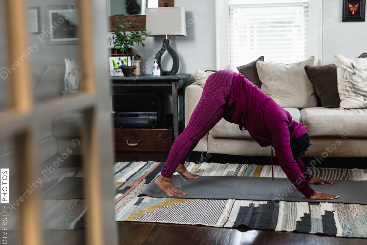 Black woman does downward dog yoga pose at home