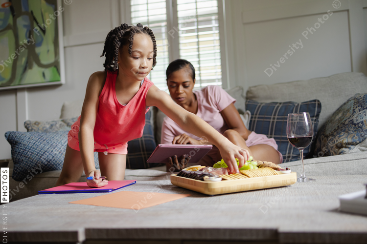 Mother and daughter spending time together in living room, girl eating snack