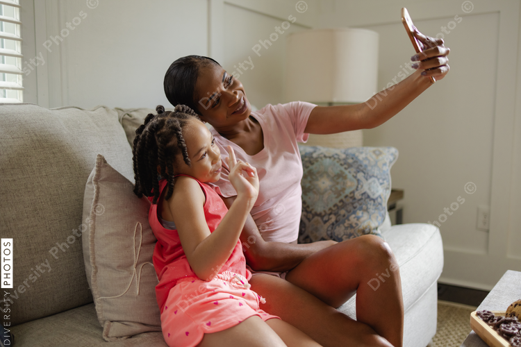Mother and daughter sitting on sofa using phone to take selfie