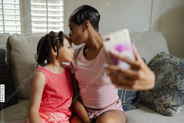 Mother and daughter sitting on sofa using phone to take selfie