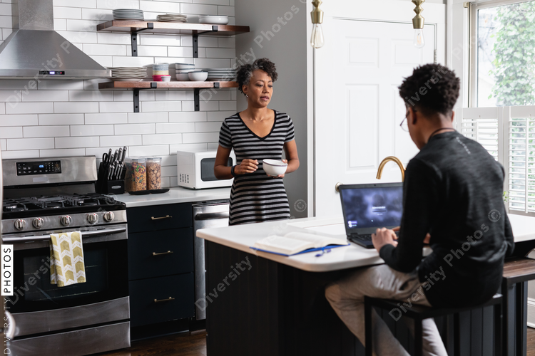 Mother preparing breakfast cereal while son studying on laptop