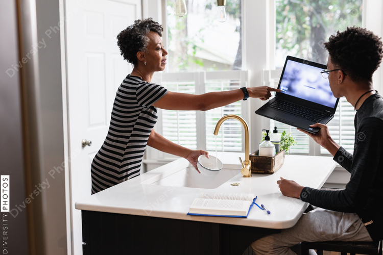 Black mother preparing breakfast cereal for son studying on laptop