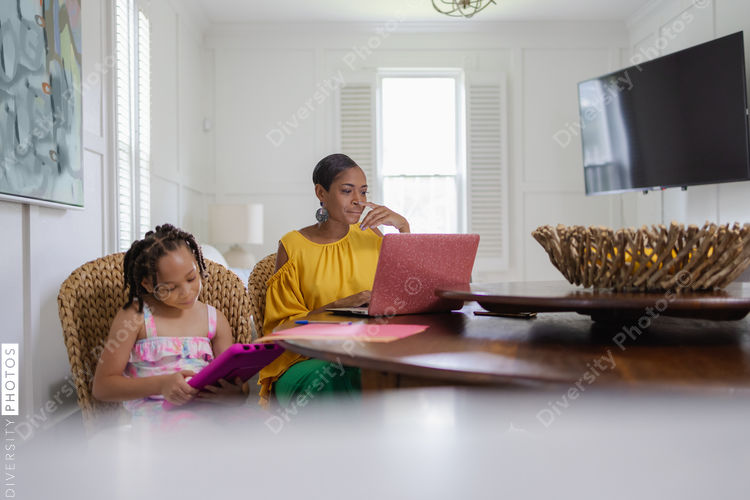 Mother using laptop, daughter using tablet in living room