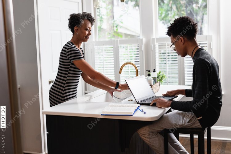 Black mother preparing breakfast cereal for son studying on laptop