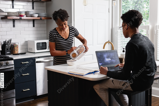 Black mother preparing breakfast cereal for son studying on laptop