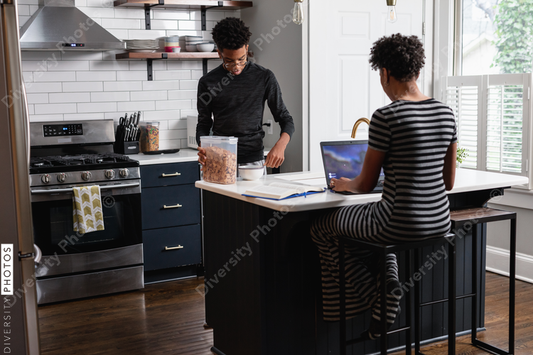 Black son prepares cereal breakfast food while mom is working on laptop
