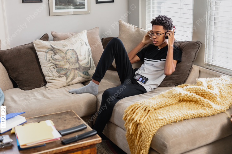 Black teen boy puts on headphones to listen to music at home, relaxed
