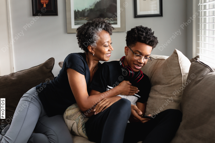 Black mother and son laughing together on couch, loving moment